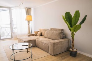Un salon avec un canapé beige, une table basse en verre, une plante en pot et un lampadaire.