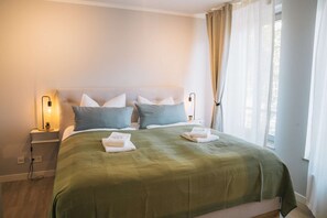 Un lit bien fait, recouvert d’une couverture verte, avec deux oreillers et deux serviettes pliées posées sur le lit.