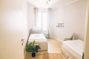 Habitación de hotel minimalista con dos camas, una planta en maceta y un perchero.