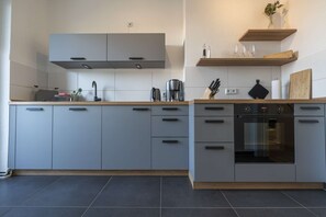 A modern kitchen with grey cabinets, a built-in oven, and a wooden countertop.
