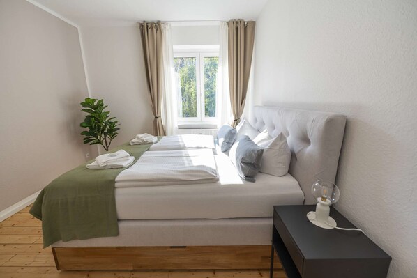 A bedroom with a bed, bedside table, lamp, and a window with curtains.