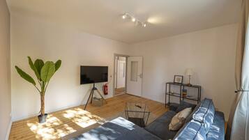 Een woonkamer met een bank, een televisie, een plant en een boekenkast.