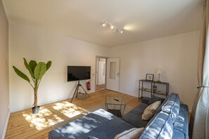 A living room with a sofa, a television, a plant, and a bookshelf.