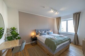 A bedroom with a bed, a desk, a chair, a window with curtains, and a plant. - RR | Central Apartment 80 m² -2 | Balcony | Washer (Magdeburg)
