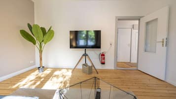 A living room with a television on a tripod stand, a potted plant, and a fire extinguisher mounted on the wall.