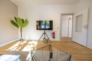 Un saló amb una televisió sobre un suport trípode, una planta en test i un extintor de foc fixat a la paret.
