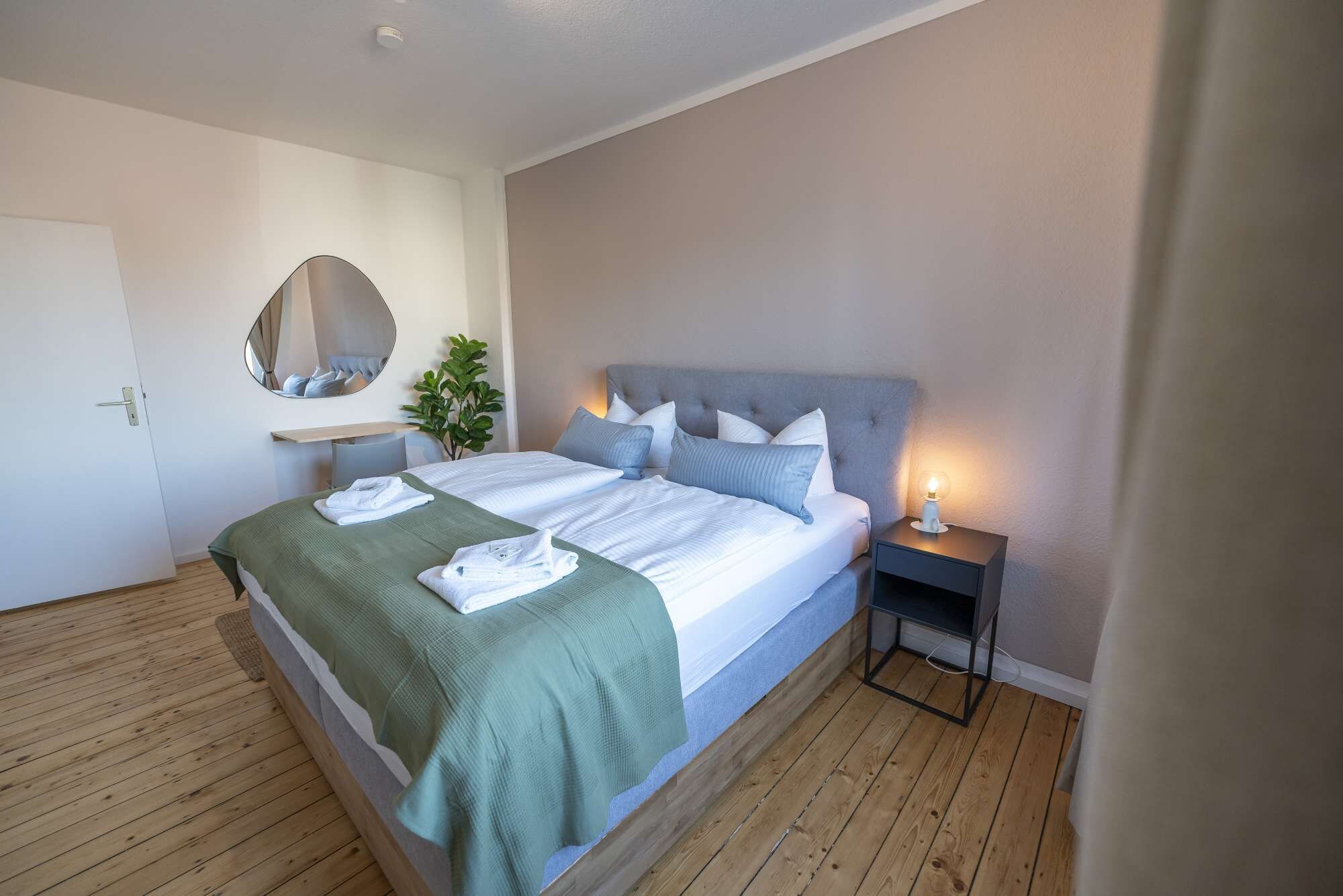 Een hotelkamer met een bed, nachtkastje en een spiegel.
