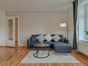 A modern living room with a grey sectional sofa, a small round coffee table, and a floor lamp. - RR | Apartments Kappel | 85 m² | Lift | WIFI (Chemnitz)