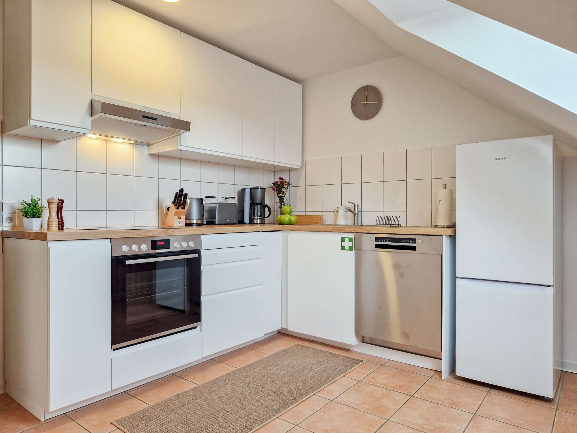 A modern kitchen with white cabinetry, a built-in oven, a dishwasher, and a stainless steel refrigerator.