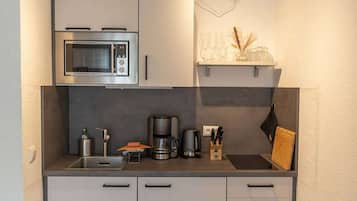 Een kleine keuken met een inbouwmagnetron, koffiezetapparaat en een klein plankje met decoratieve spullen.