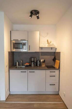 Een kleine keuken met een inbouwmagnetron, koffiezetapparaat en een klein plankje met decoratieve spullen.
