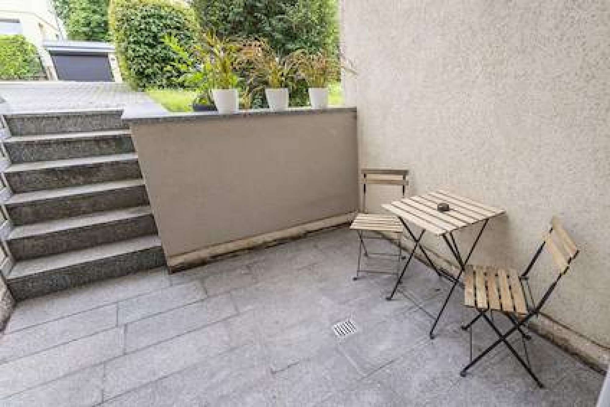 Een terras met een kleine tafel en stoelen, een trap en bloempotten.