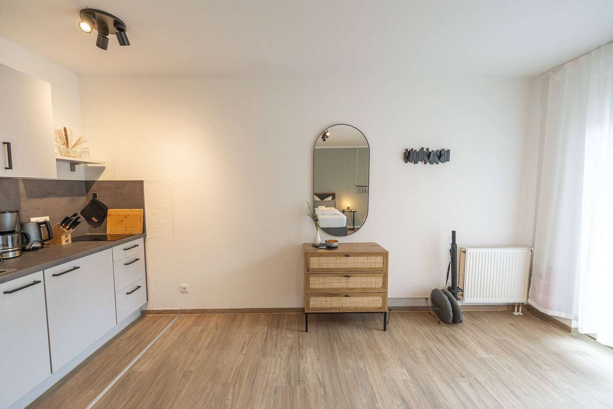 Een moderne kamer met een keukenhoekje, een houten dressoir, een spiegel en een radiator.