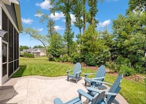 Un patio con poltrone Adirondack, un prato e una casa con veranda.