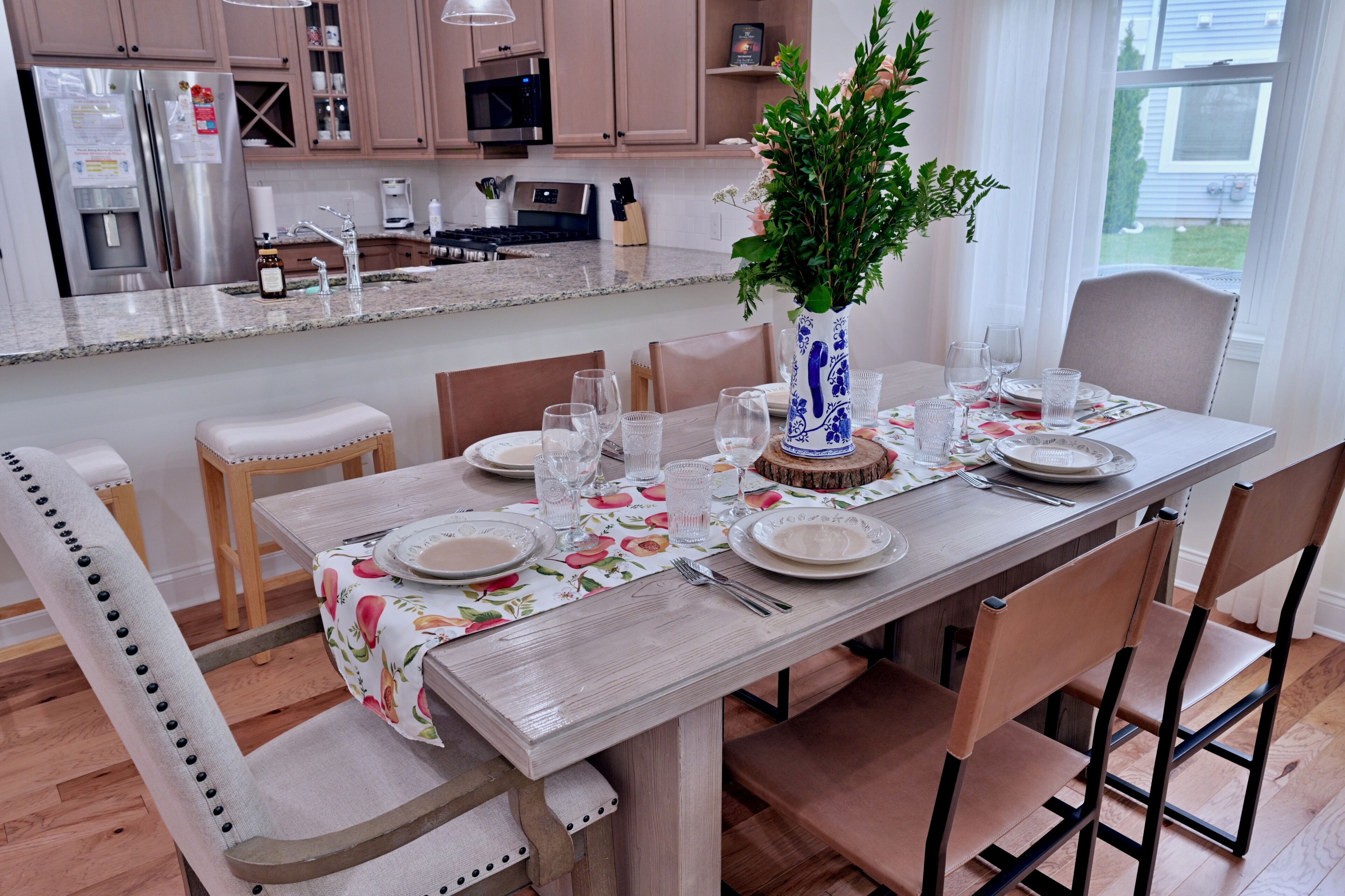 Uma sala de jantar com uma mesa de madeira posta para seis pessoas, rodeada por cadeiras, e uma cozinha ao fundo.