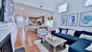 A modern living room with a blue sofa, a coffee table, and a dining area with a chandelier.
