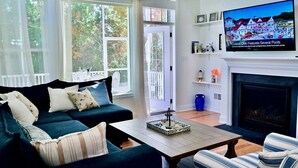 A living room with a sofa, armchair, coffee table, fireplace, TV, and large windows.