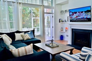 Un salon comprenant un canapé, un fauteuil, une table basse, une cheminée, un téléviseur et de grandes fenêtres.