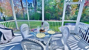 A covered patio with wicker furniture, a glass table, and a view of trees and grass.