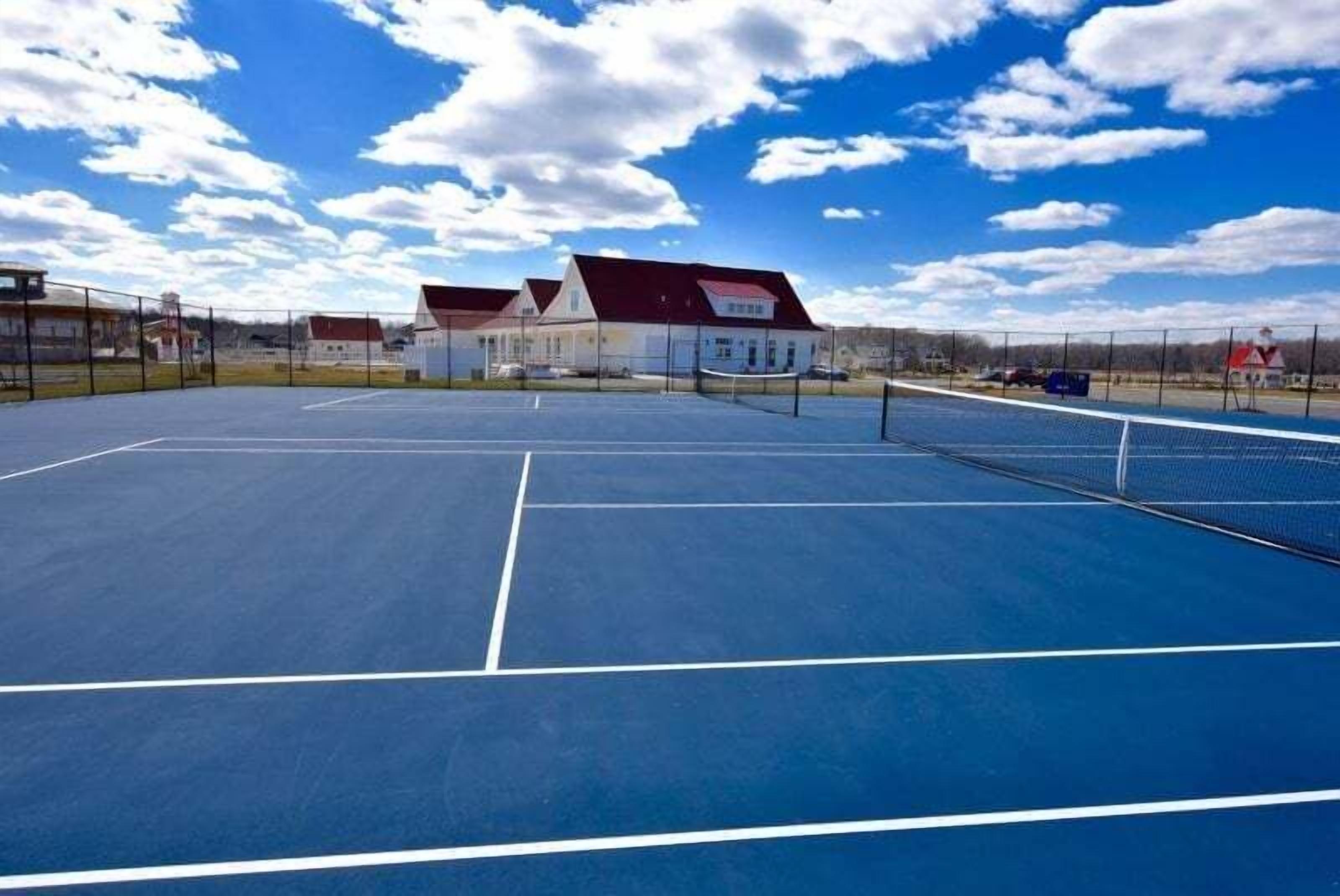 Ein Tennisplatz im Freien mit Netz, umgeben von Gebäuden mit roten Dächern.
