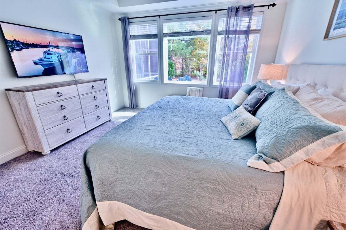 A bedroom with a bed, a dresser, a TV, and a window with a view.
