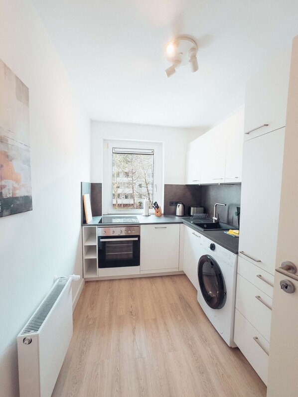 A compact kitchen with a built-in oven, a washing machine, and a window overlooking a residential area.
