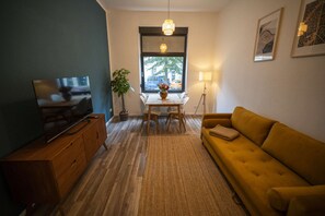 Una sala de estar con televisor, sofá, mesa de comedor y planta en maceta.