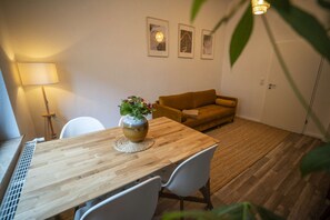 A dining area with a wooden table, white chairs, a vase with flowers, a sofa, and framed artwork on the wall. - RR | Spacious Apt_1-70 m² | Parking | Central (Magdeburg)