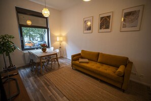 A living room with a sofa, a dining table with chairs, a lamp, a potted plant, and artwork on the wall.