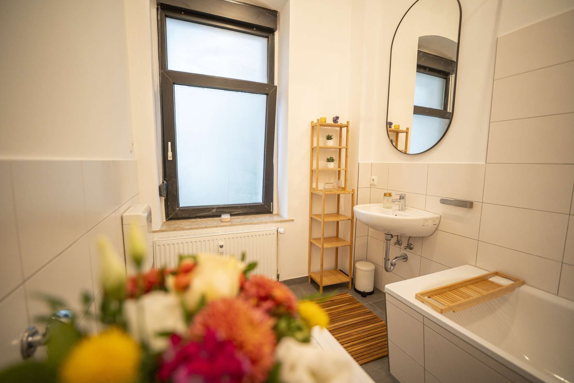 Un baño moderno con ventana, un lavamanos, un espejo y una estantería de madera.