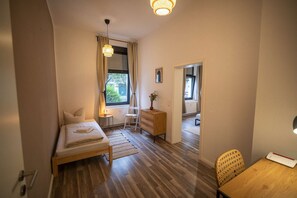 A compact bedroom with a bed, bedside table, chair, and a small table with a vase. - RR | Spacious Apt_1-70 m² | Parking | Central (Magdeburg)