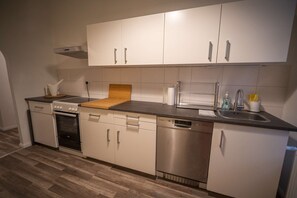 A compact kitchen with white cabinets, a dishwasher, a stove, and a sink.