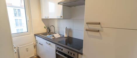 A compact kitchen with a built-in oven, a stovetop, and a window providing natural light.