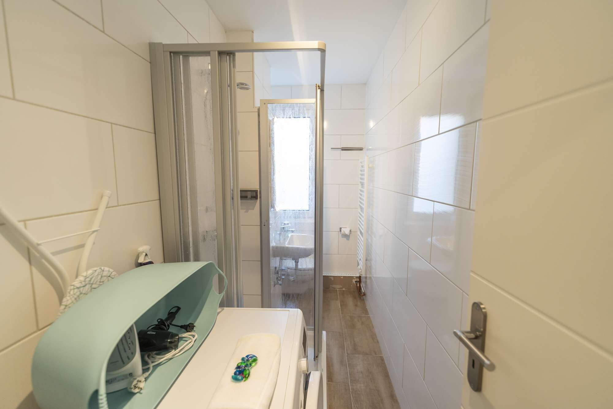 Ein schmales Badezimmer mit Dusche, Waschbecken und Handtuchhalter.