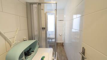 Ein schmales Badezimmer mit Dusche, Waschbecken und Handtuchhalter.