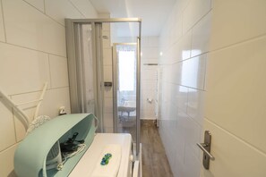 Ein schmales Badezimmer mit Dusche, Waschbecken und Handtuchhalter.