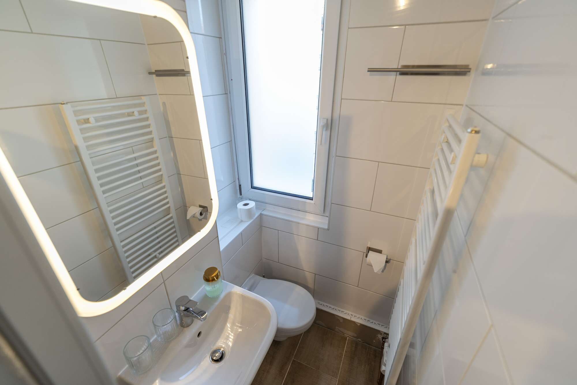 Ein Badezimmer mit einem weißen Waschbecken, einer Toilette und einem Spiegel mit Beleuchtung.