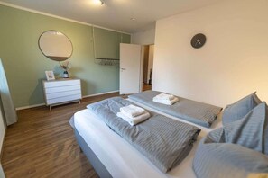 A hotel room with two beds, a dresser, a mirror, and a clock on the wall.