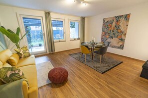 Una sala moderna con un sofá, una mesa de comedor para dos personas y un ventanal con cortinas.