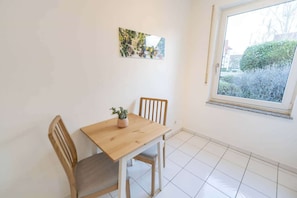 A small dining area with a wooden table and two chairs, a small potted plant, and a window with a view of a garden.