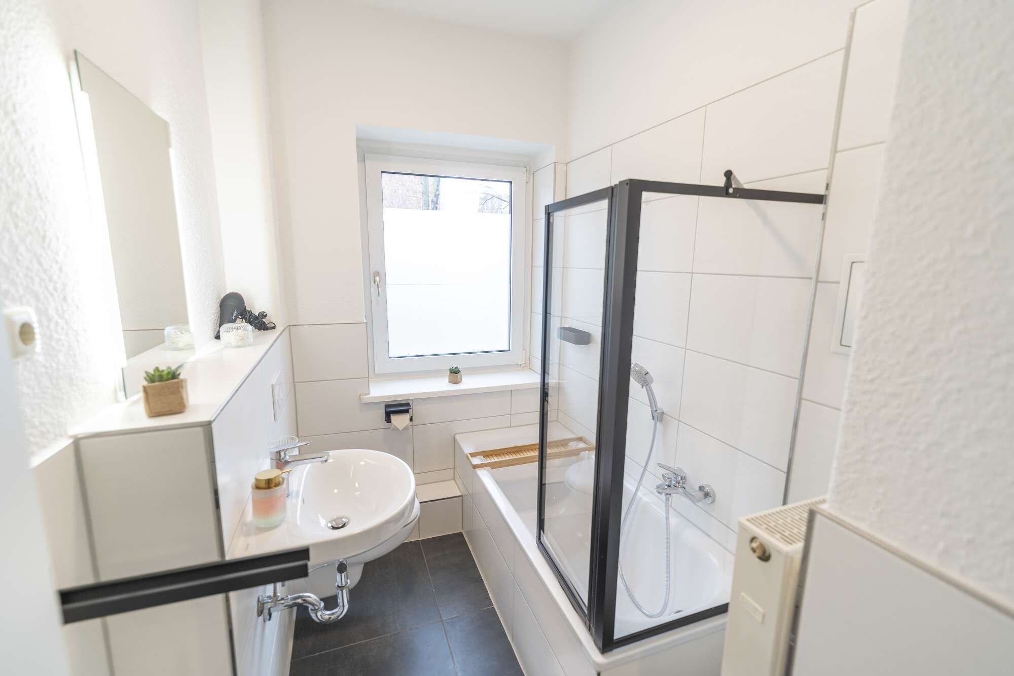 Ein Badezimmer mit einem weißen Waschbecken, einer Duschkabine und einem Fenster über dem Waschbecken.