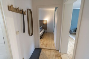 A hallway with a wooden floor, a bench, and a door leading to a room with a bed and a window with blinds. - RR | Awesome Apartment 46 m² | Kitchen | WIFI (Magdeburg)