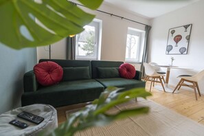 Ein Wohnzimmer mit einem grünen Sofa, einem Esstisch mit Stühlen und einem großen Fenster.