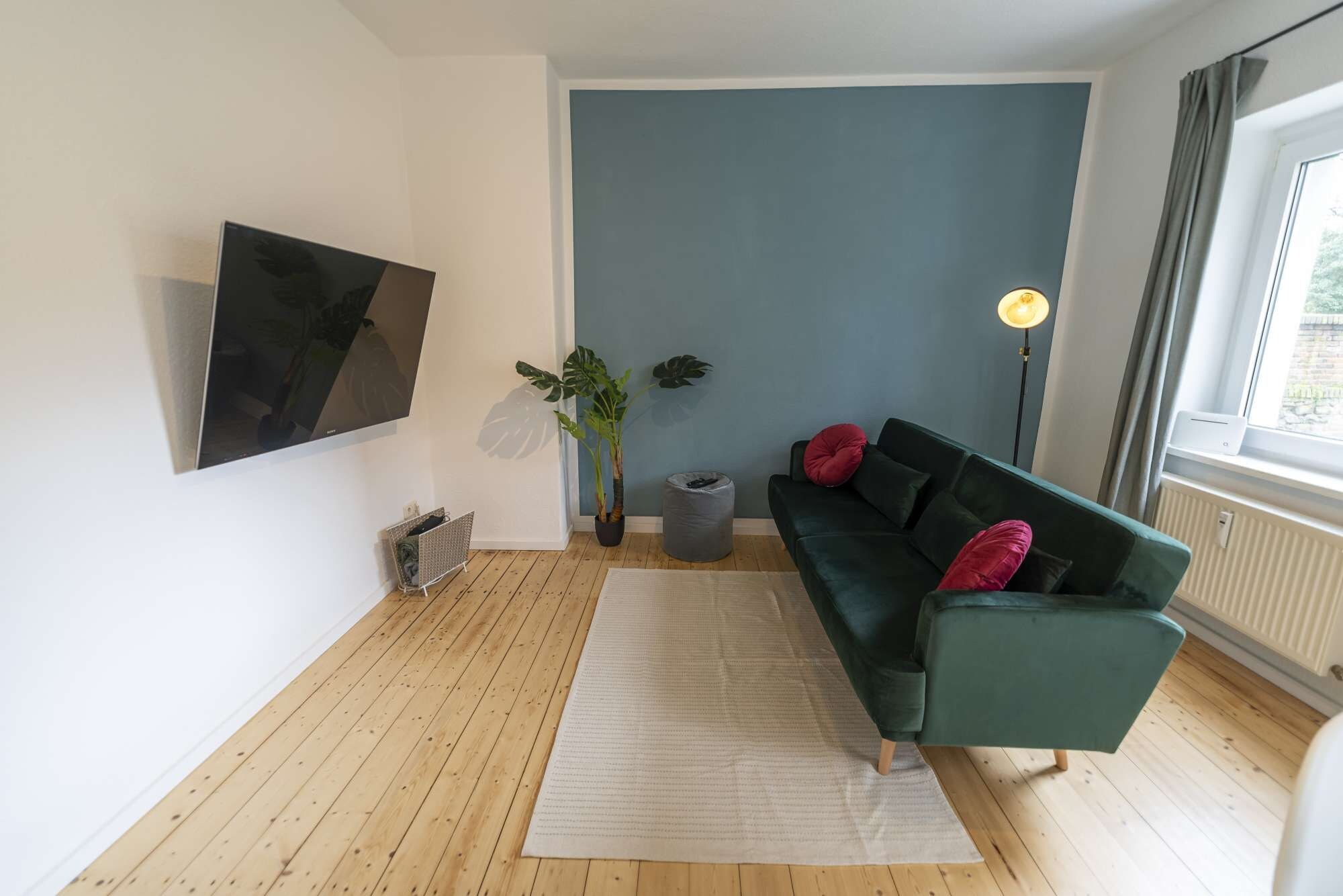 Een moderne woonkamer met een groene bank, een flatscreen televisie, een potplant en een vloerlamp.
