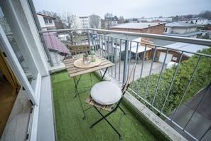 Un balcon avec une petite table, une chaise et une vue sur le quartier environnant.