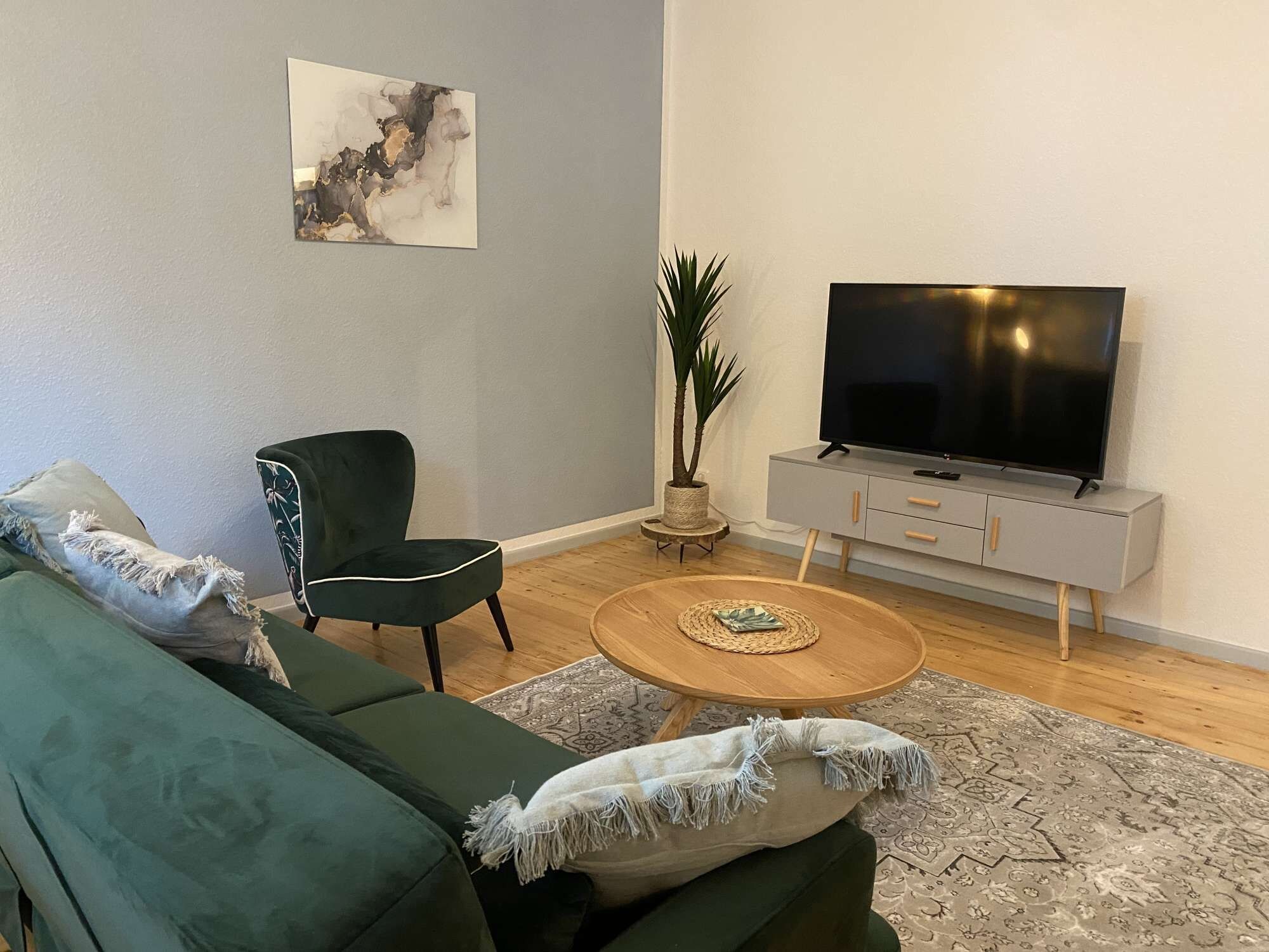 Een woonkamer met een groene bank, een fauteuil, een salontafel, een tv op een dressoir en een plant.