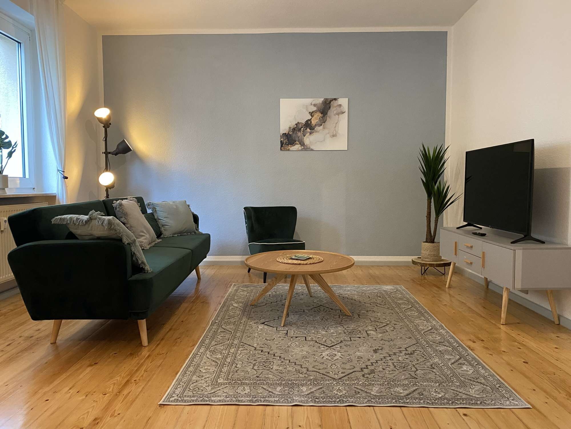 Una sala de estar con un sofá verde, una mesa de centro redonda de madera, un televisor y un cuadro en la pared.