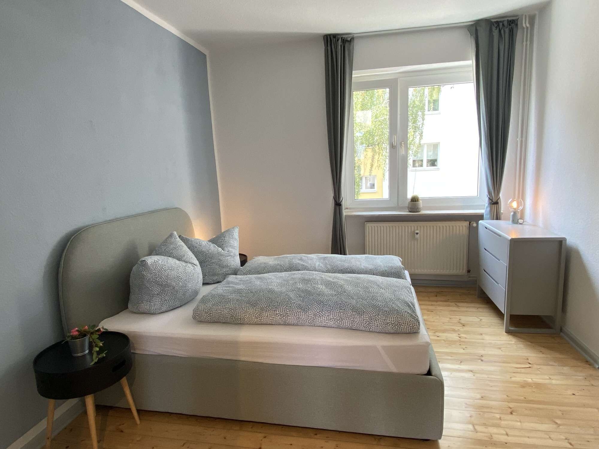 A bedroom with a bed, bedside table, and a window with curtains.