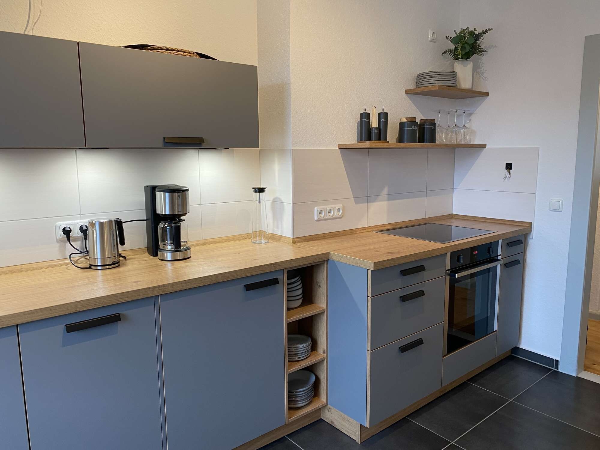 A modern kitchen with grey cabinets, a wooden countertop, a coffee maker, and a built-in oven.