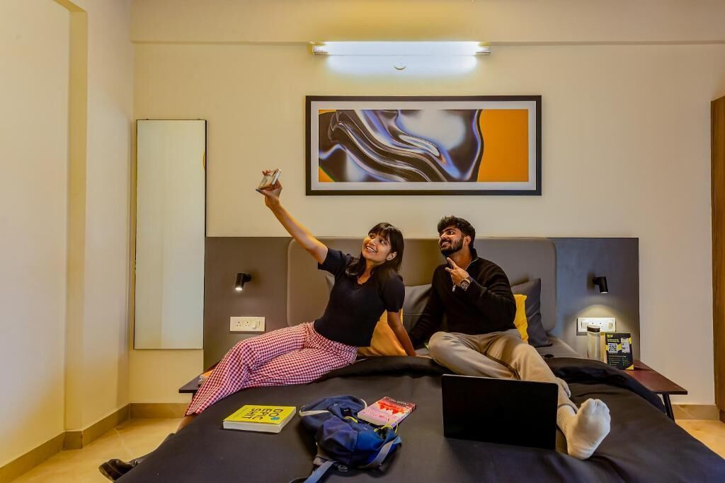 Une chambre d’hôtel moderne avec un lit, un ordinateur portable et un téléphone intelligent posés sur le lit.